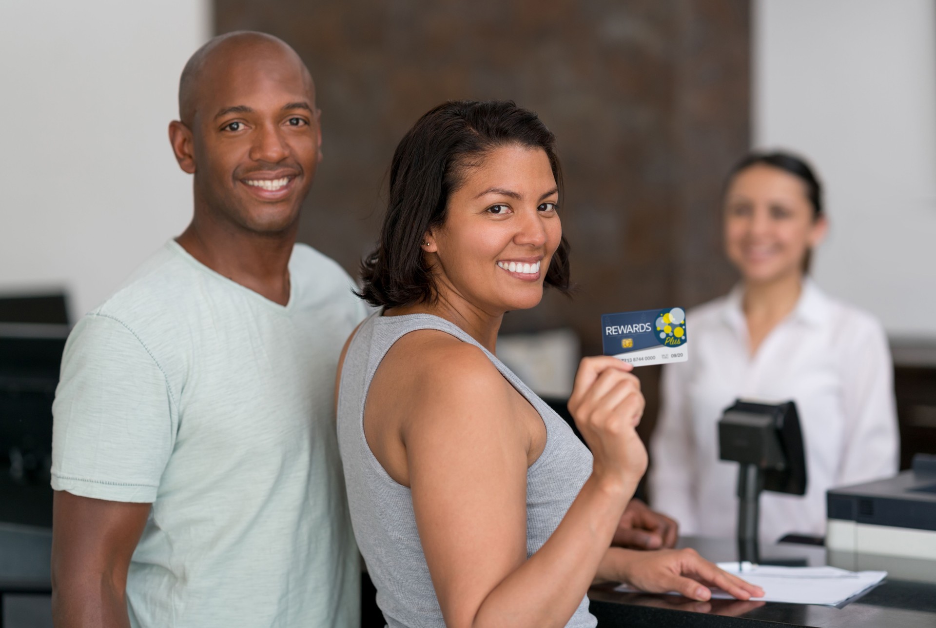 Diverse latin american couple checking in a hotel and woman holding a loyalty card all smiling at camera